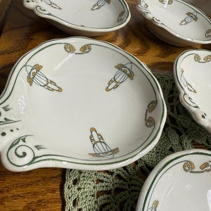 May include: A collection of white ceramic dishes with a scalloped edge and a green and gold design. The dishes have a unique shape and are decorated with a repeating geometric pattern. The dishes are arranged on a wooden surface.