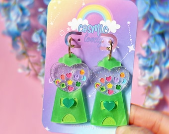 May include: A pair of green gumball machine earrings with a heart-shaped window filled with colorful candies. The earrings are on a card that says "cosmic lovely" and "cosmiclovely.com".