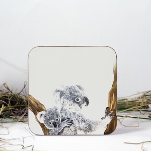 May include: A square coaster with a brown wooden frame and a white background. The coaster features a hand-painted illustration of two koalas, one adult and one baby, on a tree branch.