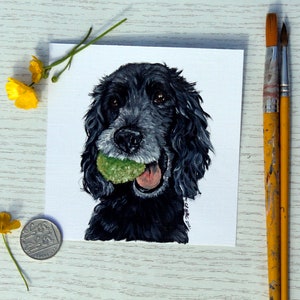 以下が含まれることがあります： 口に緑色のボールを持った黒い犬の絵。犬は舌を出して鑑賞者を見ている。