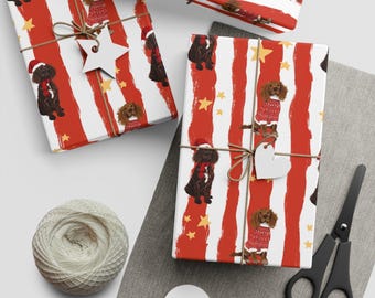 Puede incluir: Papel de regalo navideño con rayas rojas y blancas, adornado con ilustraciones de perros con atuendos festivos y estrellas doradas. Los regalos envueltos están atados con hilo y etiquetas de madera en forma de estrella y corazón. También hay un ovillo de hilo y tijeras.