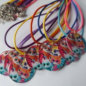 Puede incluir: Un conjunto de collares coloridos con colgantes redondos, coloridos, con personajes de gatos de dibujos animados. Los colgantes presentan un grupo de gatos con trajes de superhéroes.