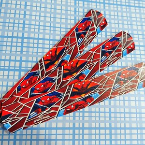 Peut inclure: Trois bandes de tissu rouge et bleu avec un motif Spider-Man. Les bandes ont un fond blanc avec un motif de toile rouge et des images de Spider-Man. Le texte "Spider-Man" est imprim&eacute; sur chaque bande.