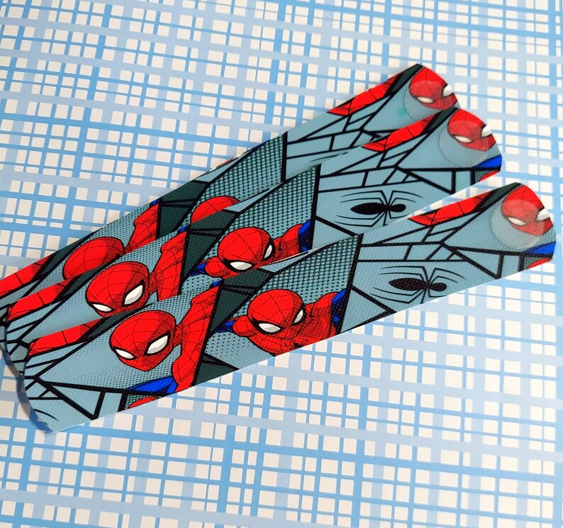Peut inclure: Trois bandes de tissu bleu et gris &agrave; motifs avec une image de style bande dessin&eacute;e de Spiderman en rouge et bleu. Les bandes sont superpos&eacute;es.