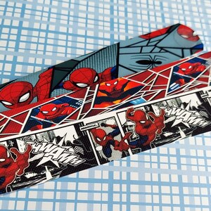 Peut inclure: Trois bandes de tissu rouge, noir et blanc avec un motif de bande dessin&eacute;e mettant en sc&egrave;ne Spiderman. Les bandes pr&eacute;sentent un motif r&eacute;p&eacute;t&eacute; de Spiderman dans diff&eacute;rentes poses et les mots "Wham!" et "Pow!" dans une police de caract&egrave;res de bande dessin&eacute;e.