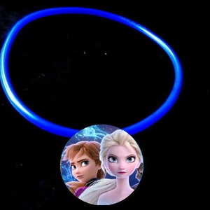 May include: A blue glow stick necklace with a round pendant featuring a picture of Elsa and Anna from the movie Frozen.