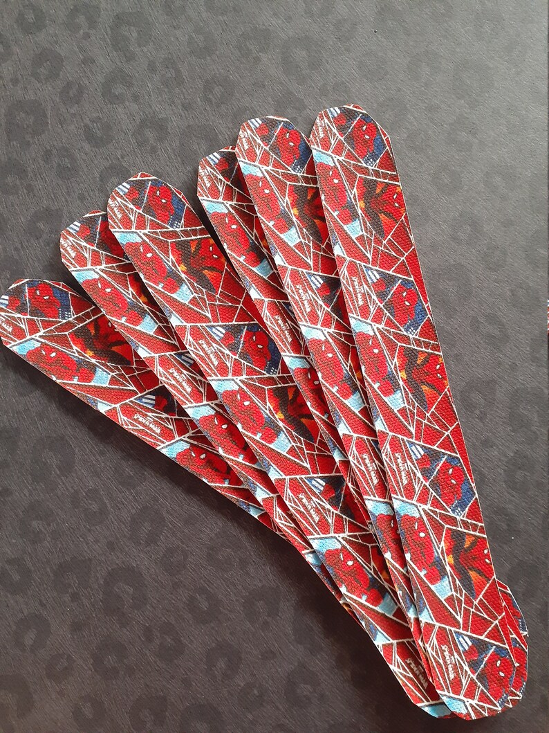 Peut inclure: Six bracelets en tissu rouge, bleu et blanc avec un motif Spiderman. Les bracelets sont dispos&eacute;s en &eacute;ventail.