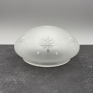 May include: A dome-shaped glass light fixture shade with a frosted finish. The surface features a repeating pattern of clear, etched eight-pointed starburst designs interspersed with small, raised circular dots around the rounded exterior.