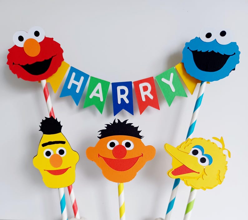 May include: A Sesame Street themed cake topper set with Elmo, Cookie Monster, Big Bird, and Bert. The set includes a banner that says "HARRY".
