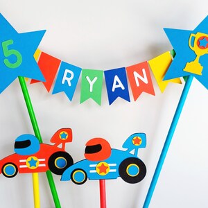 Bright primary coloured bunting cake topper with stripy straws.  2 stars either side of the bunting displaying the age in one star and a trophy in the other.  This topper comes complete with 2 racing cars.