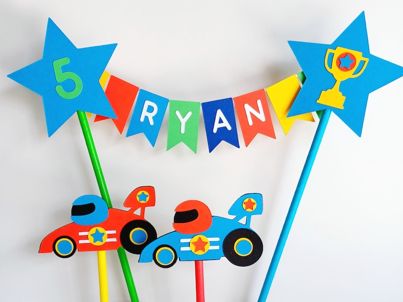 Bright primary coloured bunting cake topper with stripy straws.  2 stars either side of the bunting displaying the age in one star and a trophy in the other.  This topper comes complete with 2 racing cars.