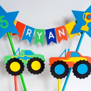 Personalised, Bunting cake topper.  Bright primary coloured bunting with 2 monster trucks.  One green and one red.   A trophy in a star on one side of the topper and the age of the birthday boys in a star on the other side.  Fabulous cake decoration.