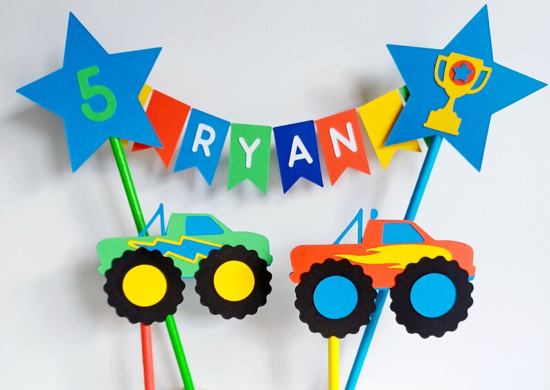 Personalised, Bunting cake topper.  Bright primary coloured bunting with 2 monster trucks.  One green and one red.   A trophy in a star on one side of the topper and the age of the birthday boys in a star on the other side.  Fabulous cake decoration.