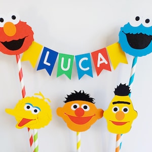 May include: A cake topper set featuring Sesame Street characters, including Elmo, Cookie Monster, Big Bird, and Bert and Ernie. The set includes a banner that reads "LUCA".