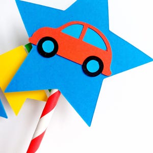 May include: A red car cutout with blue windows and black wheels is attached to a blue star. The star is part of a decorative item, with a red and white striped straw. A yellow star is also visible.
