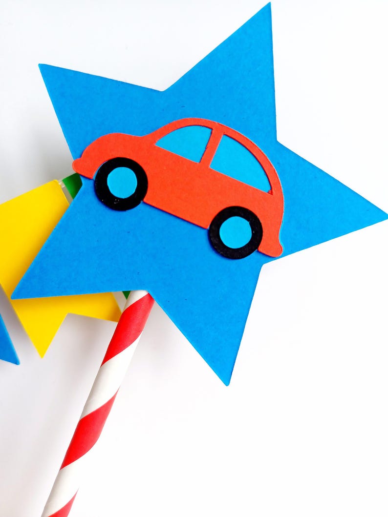 May include: A red car cutout with blue windows and black wheels is attached to a blue star. The star is part of a decorative item, with a red and white striped straw. A yellow star is also visible.