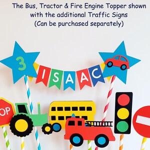 May include: Colorful birthday cake toppers featuring a bus, tractor, and fire engine. The toppers include a banner spelling "ISAAC", a star with the number "3", and various traffic signs. The text "The Bus, Tractor & Fire Engine Topper shown with the additional Traffic Signs (Can be purchased separately)" is also visible.
