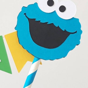 May include: Blue and black Cookie Monster cake topper with white eyes and a striped blue and white straw.
