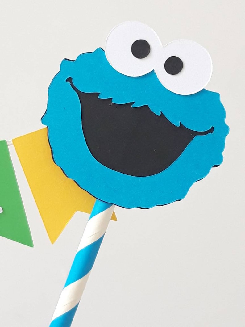 May include: Blue and black Cookie Monster cake topper with white eyes and a striped blue and white straw.