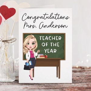 May include: A white card with the text "Congratulations Mrs. Anderson Teacher of the Year" and a cartoon illustration of a blonde woman standing in front of a chalkboard with the same text.