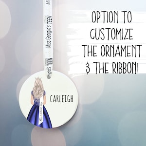 以下が含まれることがあります： 白い丸いオーナメントに、青と白の女性がドレスを着たイラストが描かれています。オーナメントは、「Miss Georgia's TEEN OUTSTANDING」という文字が書かれた白いリボンに吊り下げられています。オーナメントには「CARLEIGH」という文字が書かれています。「OPTION TO CUSTOMIZE THE ORNAMENT & THE RIBBON!」という文字が白い背景に書かれています。
