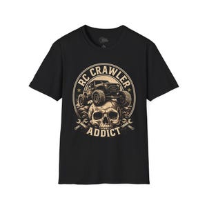 Puede incluir: Una camiseta negra de manga corta con un estampado gráfico de una calavera con un vehículo RC crawler encima. El diseño está encerrado en un borde circular con el texto RC CRAWLER ADDICT y dos llaves inglesas cruzadas en la parte inferior en beige.