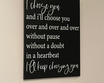 May include: A rectangular black wall sign featuring white text that reads: I choose you and I'll choose you over and over and over without pause without a doubt in a heartbeat I'll keep choosing you. The sign has a clean, flat surface.
