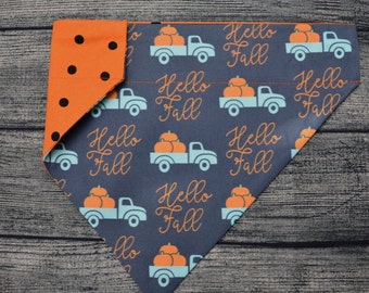 May include: A blue and orange reversible dog bandana with a pattern of trucks carrying pumpkins and the text "Hello Fall". One side of the bandana is solid orange with white polka dots.