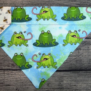 May include: A blue and green bandana with a pattern of frogs with their tongues sticking out. The bandana is folded in half and has a white border with a bee pattern.