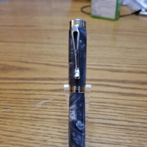 May include: A silver and black pen with a swirl pattern on the barrel. The pen has a gold band near the top and bottom of the barrel.