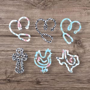 以下が含まれることがあります： ハート、十字架、鶏、テキサス、そして2種類の聴診器の形をした、6種類の異なる模様の金属製ヘアクリップ。模様には、花柄、レオパード柄、青と白の花柄が含まれています。