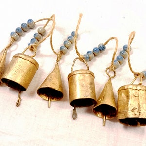 May include: A set of six gold-coloured bells with blue and white beads strung on twine. The bells are of various shapes and sizes, and each has a small loop at the top for hanging.