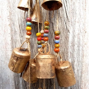 Peut inclure: Un carillon avec plusieurs cloches dorées et des perles colorées. Les cloches sont suspendues à une surface en bois.