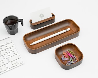 May include: A wooden desk organizer set with three pieces: a rectangular tray with a white stylus, a square bowl with colorful paper clips, and a card holder. The set is on a white surface next to a white keyboard.