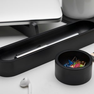 Pode incluir: Um organizador de mesa preto com dois compartimentos. O compartimento maior cont&eacute;m uma caneta prateada e o compartimento menor cont&eacute;m alfinetes coloridos.