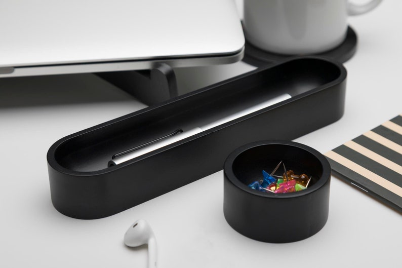 Pode incluir: Um organizador de mesa preto com dois compartimentos. O compartimento maior cont&eacute;m uma caneta prateada e o compartimento menor cont&eacute;m alfinetes coloridos.