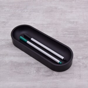 Pode incluir: Um porta-canetas oval preto com duas canetas dentro. Uma caneta &eacute; prateada com uma tampa verde, e a outra caneta &eacute; preta com uma tampa verde.