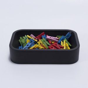May include: A black rectangular tray filled with colorful wooden clothespins. The clothespins are in shades of blue, green, yellow, red, and pink.
