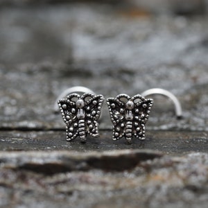 May include: Two silver butterfly nose rings. The butterfly design is detailed and intricate.