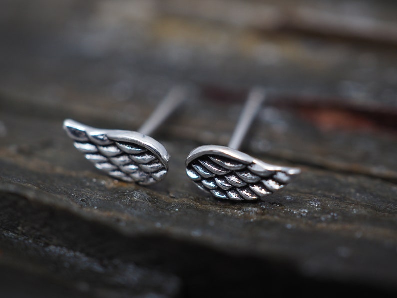 May include: A pair of silver wing-shaped stud earrings. The wings are detailed with a textured pattern.