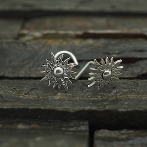 May include: Two silver nose rings with a starburst design. Each ring has a small round centre.