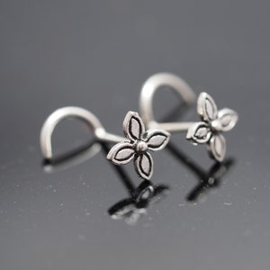 Puede incluir: Dos anillos de nariz plateados con un diseño de flor. Los anillos son de metal y tienen un aspecto simple y elegante.
