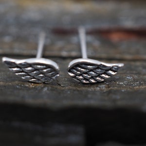 May include: A pair of silver wing-shaped stud earrings. The wings are detailed with a textured pattern.