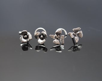 May include: Three silver nose rings with flower designs. The rings are all different shapes and sizes.