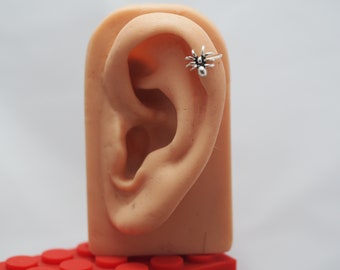 May include: A silver spider ear cuff. The spider is detailed with eight legs and a body. The ear cuff is worn on a model's ear.