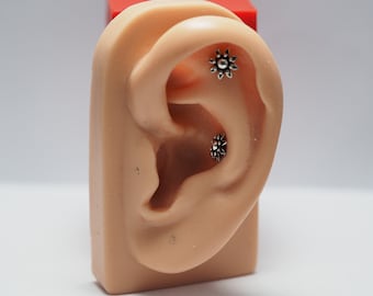 May include: A close-up of a fake ear with two silver star-shaped earrings. The earrings are small and have a delicate design.