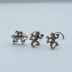 Peut inclure: Trois anneaux de nez en argent avec un motif de gecko. Les geckos sont détaillés avec des points et ont une queue recourbée.
