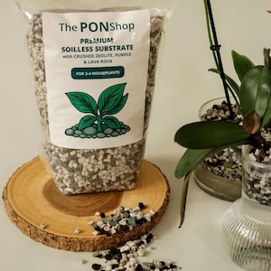 May include: A clear bag of "The PONShop" premium soilless substrate for houseplants, with crushed zeolite, pumice, and lava rock. The bag sits on a wooden slice, with an orchid and other plants in the background.