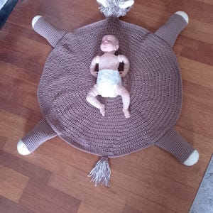 May include: A brown crocheted horse playmat with a white tail and white accents on the hooves. A baby is lying on the playmat.