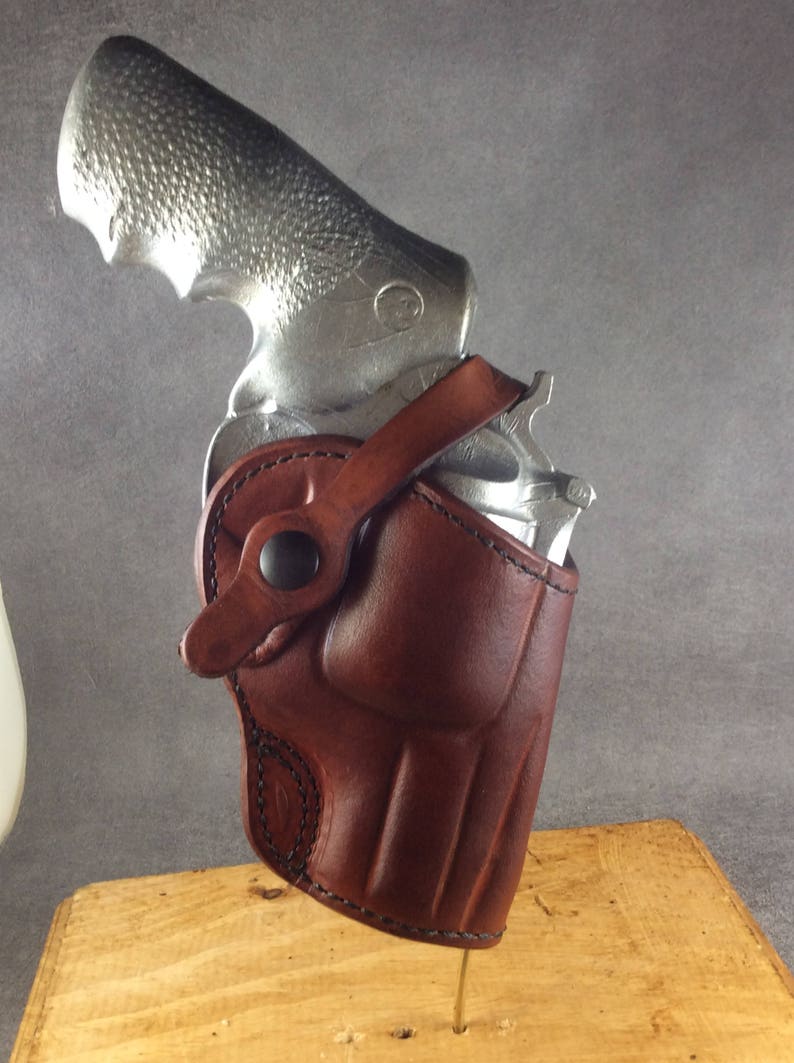 May include: A brown leather holster with a snap closure and a belt loop. A silver revolver is inside the holster.